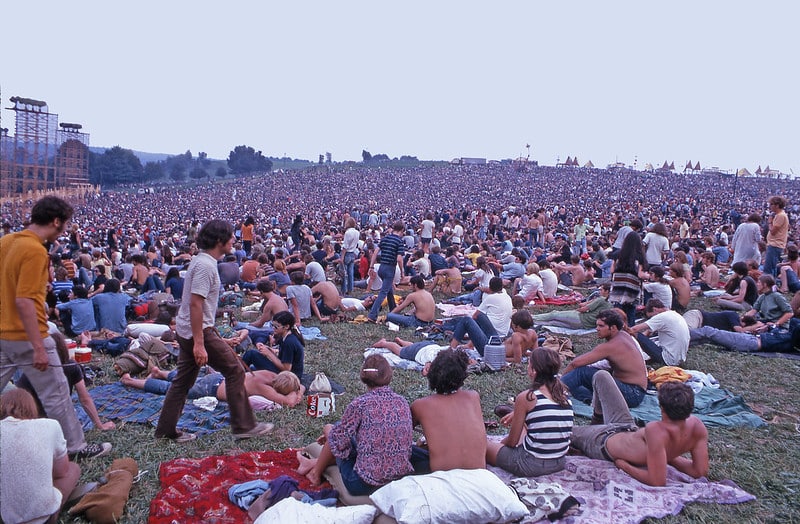 The overlooking shot of 400,000 attendees of Woodstock festival in 1969. Some have laid blankets and pillows on the field to to lounge around before the show starts