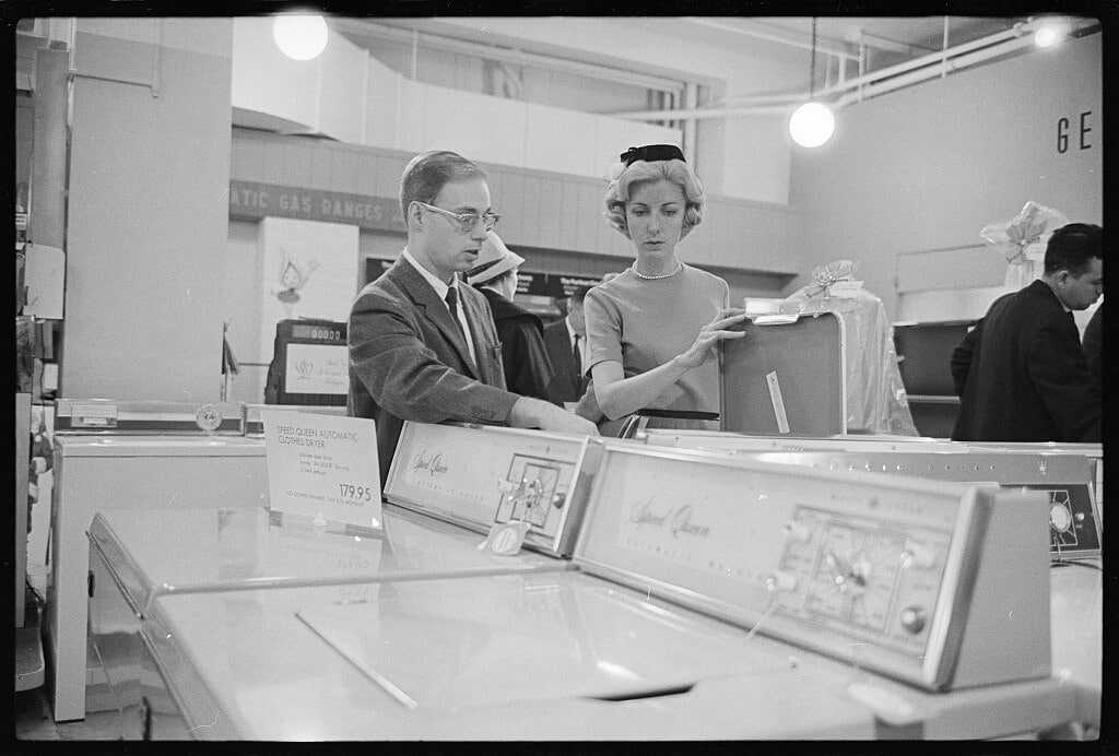 Christmas shopper looking at a Speed Queen automatic clothes dryer in a department store, possibly with a salesperson (December 1963)