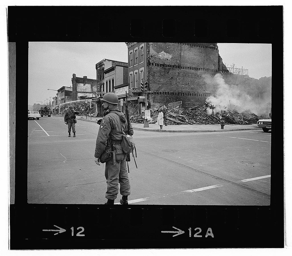 D.C. riot. April '68. Aftermath — Photograph showing a soldier standing guard in a Washington, D.C., street with the ruins of buildings that were destroyed during the riots that followed the assassination of Martin Luther King, Jr. (1968 Apr. 8)