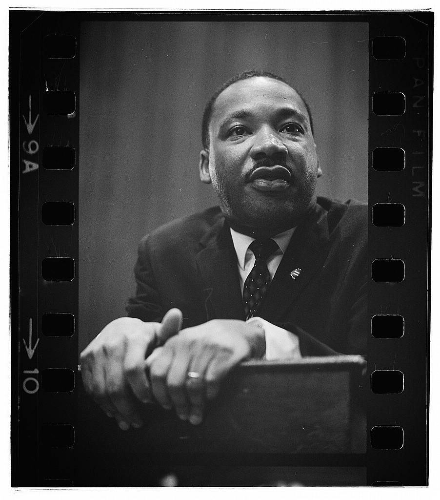 Martin Luther King press conference — Photograph shows head-and-shoulders portrait of King leaning on a lectern. (1964 Mar. 26)