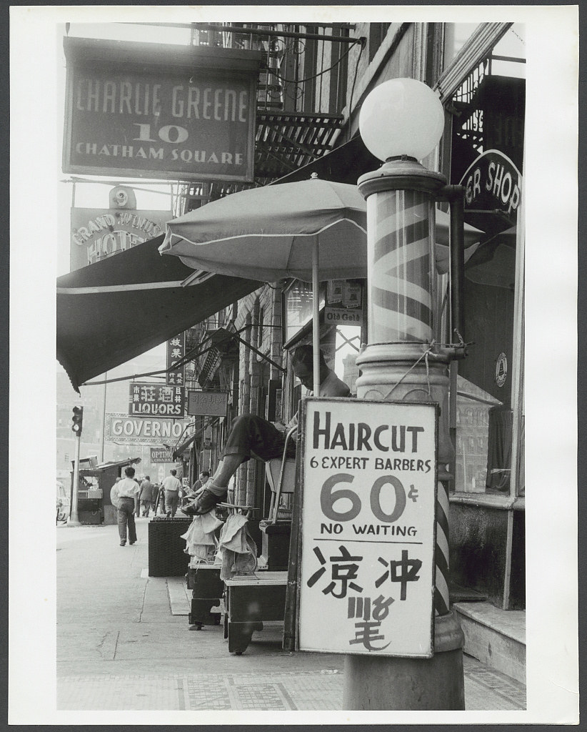 Businesses along Chatham Square, Chinatown- Photograph shows signs for businesses along Chatham Square, including a barber shop, liquor store, hotel, and Charlie Green. (July 1956)