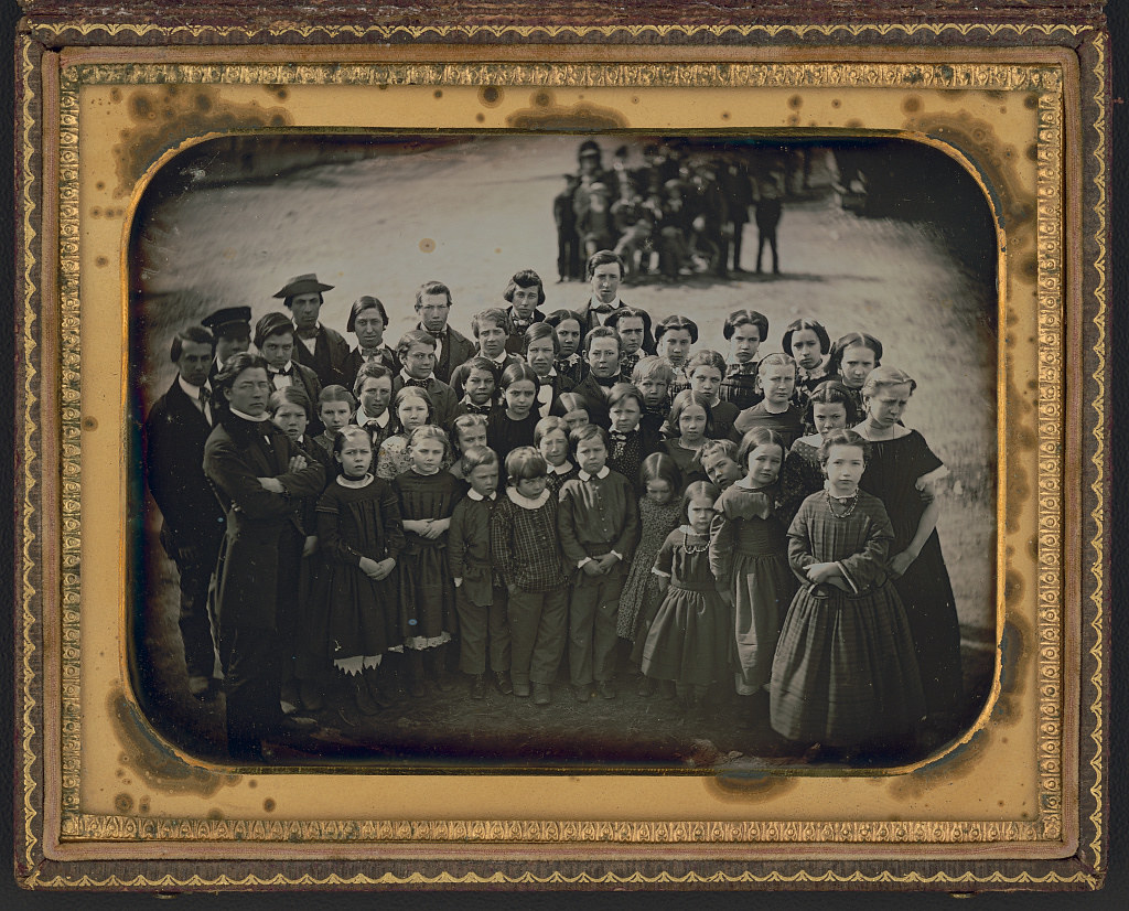 Large group of school children, with their teacher, standing in a town street (ca. 1850s)