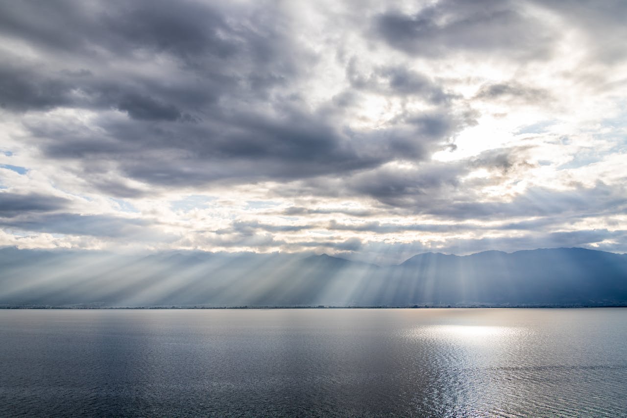 Dramatic sun rays over a lake with layered clouds.