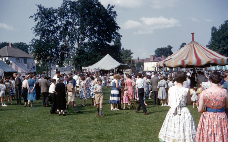 people in colorful clothing in an open field during a carnival at midday, 1960s