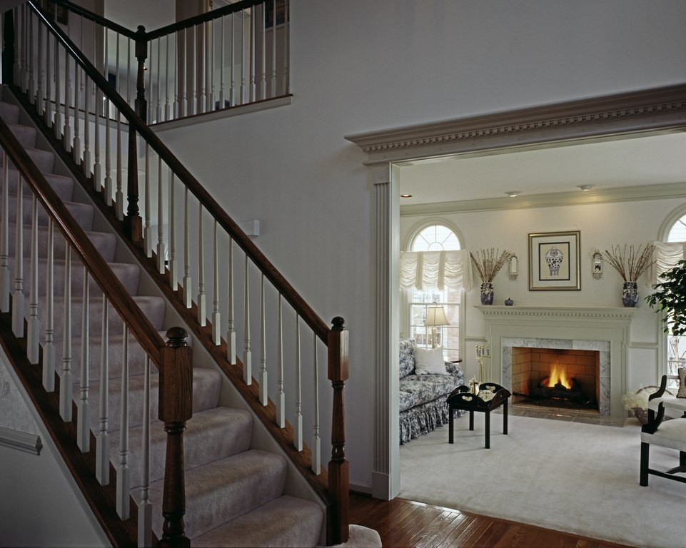 A photo of a house interior in the 80s featuring a portion of the wooden stairs and the living room with the fireplace area