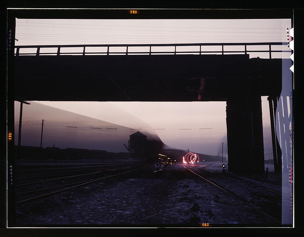 View in a departure yard at C & NW RR's Proviso yard at twilight, Chicago, Ill. Brakeman is signaling with a red flare and the train is going by during exposure (1942 Dec.)
