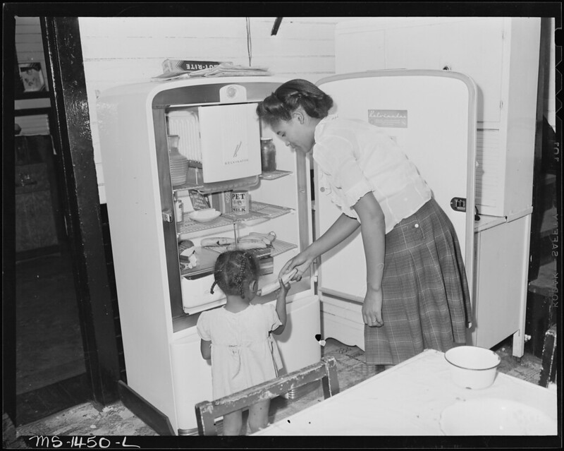 Mrs. Howard giving daughter a banana from electric fridge.