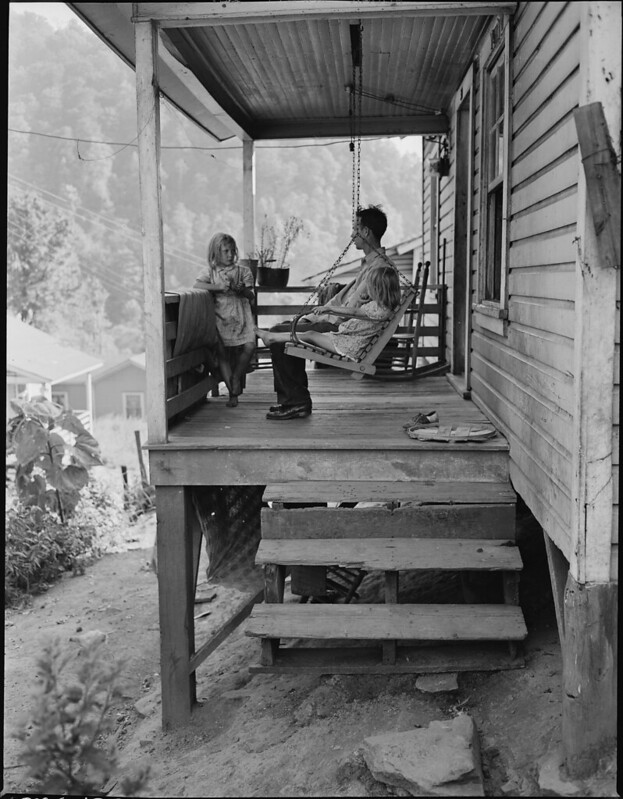 Bill Daniels, a miner, and his two daughters on the front porch of their three room house for which they pay  monthly.